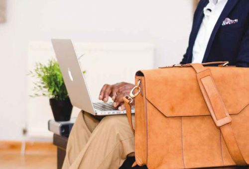 Man uses a laptop, leather satchel bag in front of him