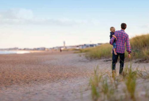 Man carries his child down a sand dune on the beach