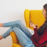 Woman relaxing on a yellow sofa using her phone