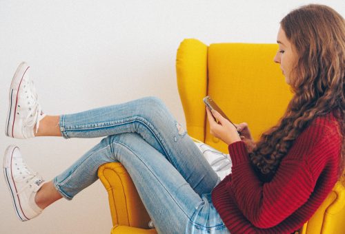 Woman relaxing on a yellow sofa using her phone